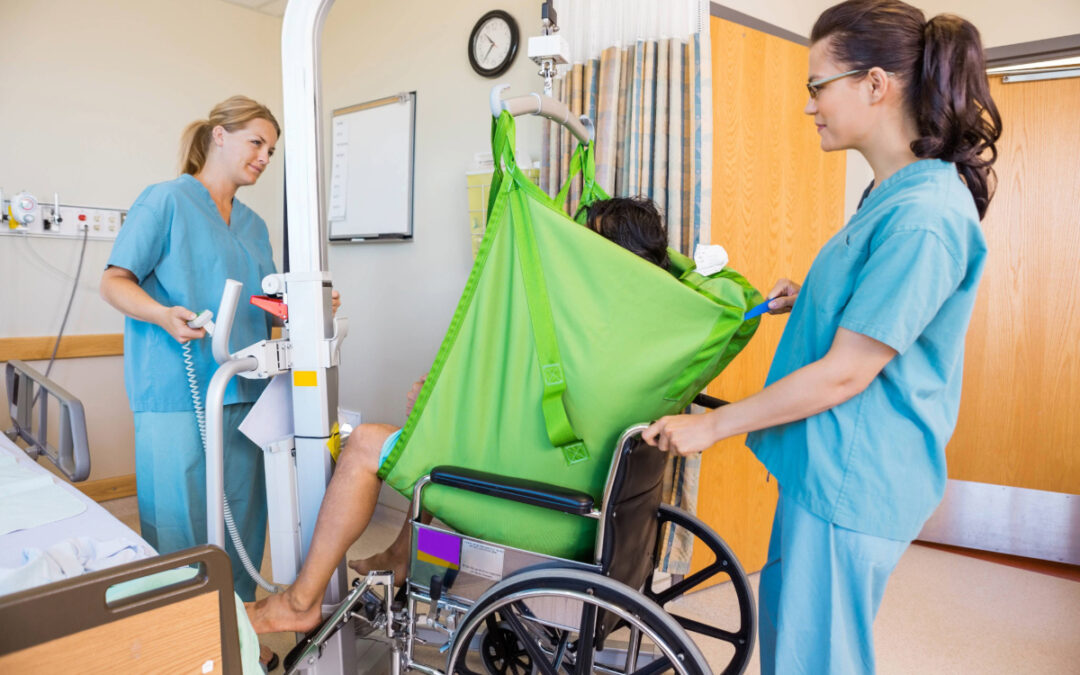 A patient in a wheelchair receives assistance to move from the hospital bed
