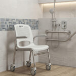 Well-maintained mobile bath chair with armrests and wheels inside a tiled accessible bathroom with safety grab bars.