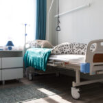 Adjustable electric hospital bed with an overhead trapeze bar and IV pole set up in a residential bedroom for long-term home care.