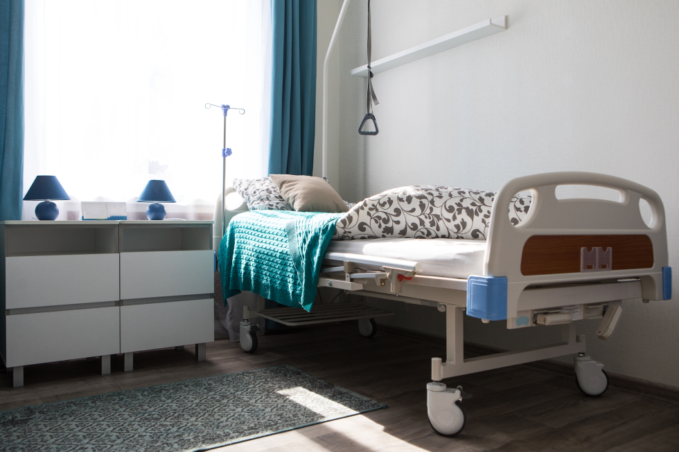 Adjustable electric hospital bed with an overhead trapeze bar and IV pole set up in a residential bedroom for long-term home care.