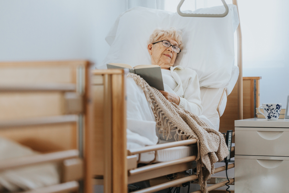 Senior woman relaxing and reading in an electric adjustable hospital bed designed for comfortable home care.